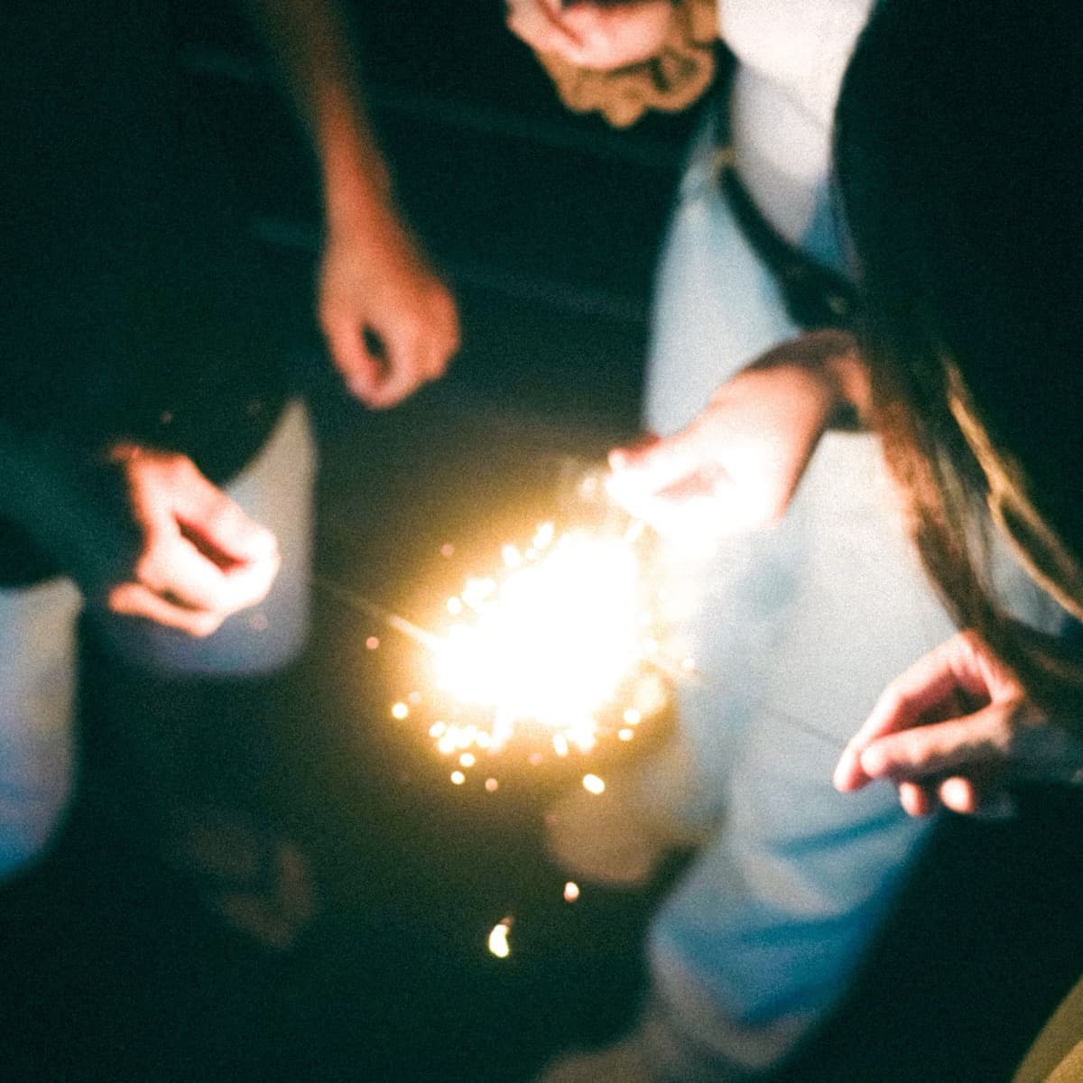 Hands holding sparklers, out of focus, in the dark
