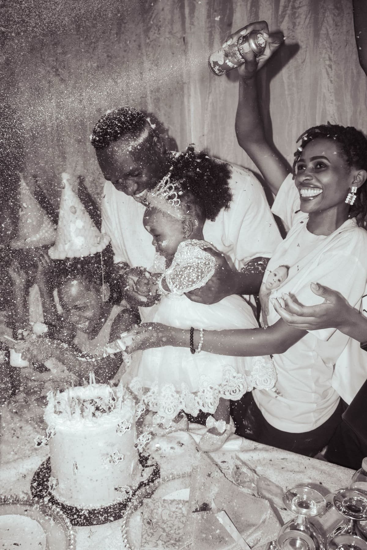 A family cutting a birthday cake in black and white, party hats on